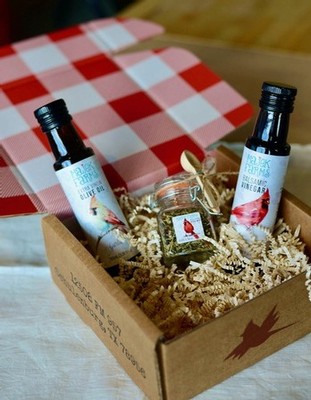 Two mini bottles of olive oil, balsamic vinegar, and a jar of dipping spice mix are inside a cardboard box. 