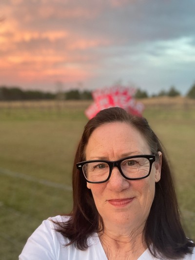 A smiling woman with eyeglasses in a field.